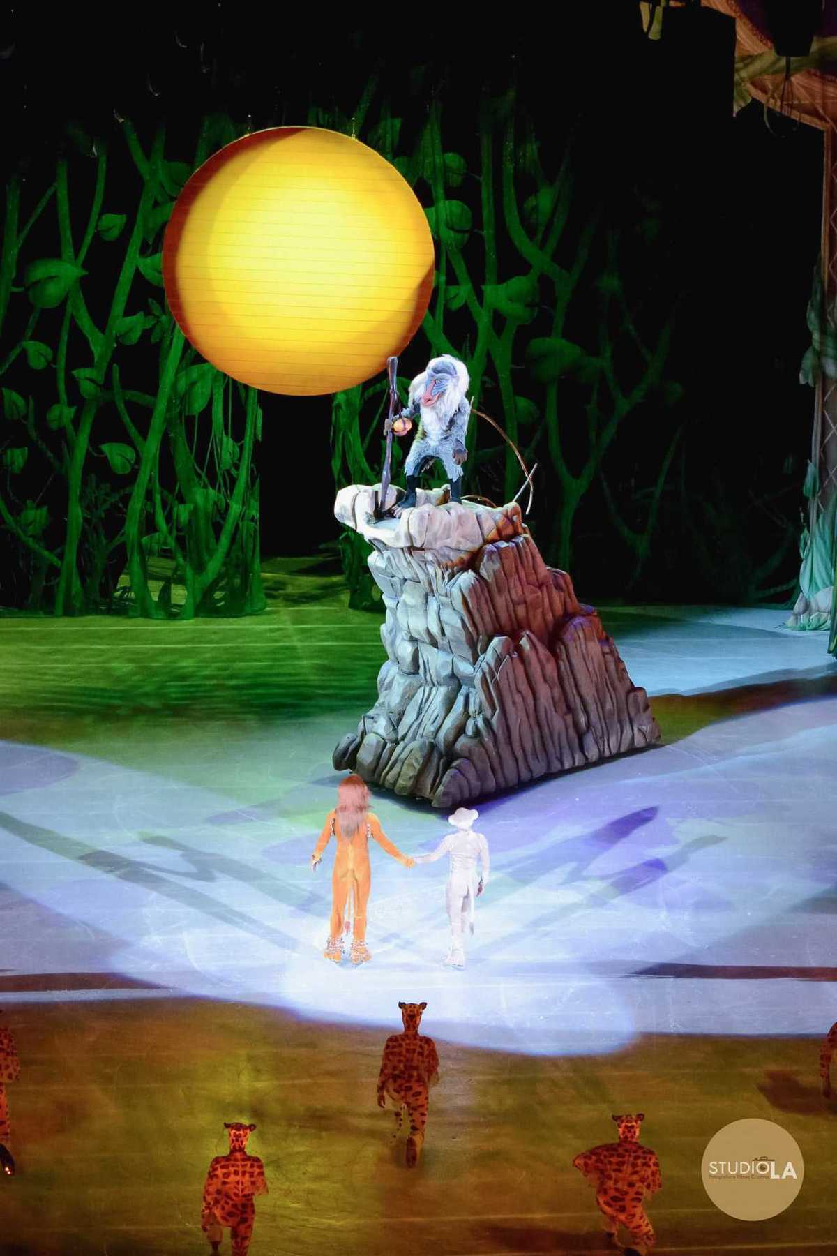 Fotografia impactante de espetáculo com personagem Rafiki erguendo o cajado em cena de O Rei Leão — registro de apresentação teatral pelo Studio LA.