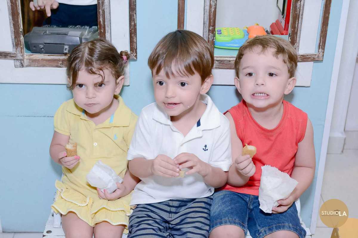 Três crianças lado a lado, aproveitando o lanche com expressões espontâneas que traduzem a alegria da festa infantil. Foto capturada pelo Studio LA.