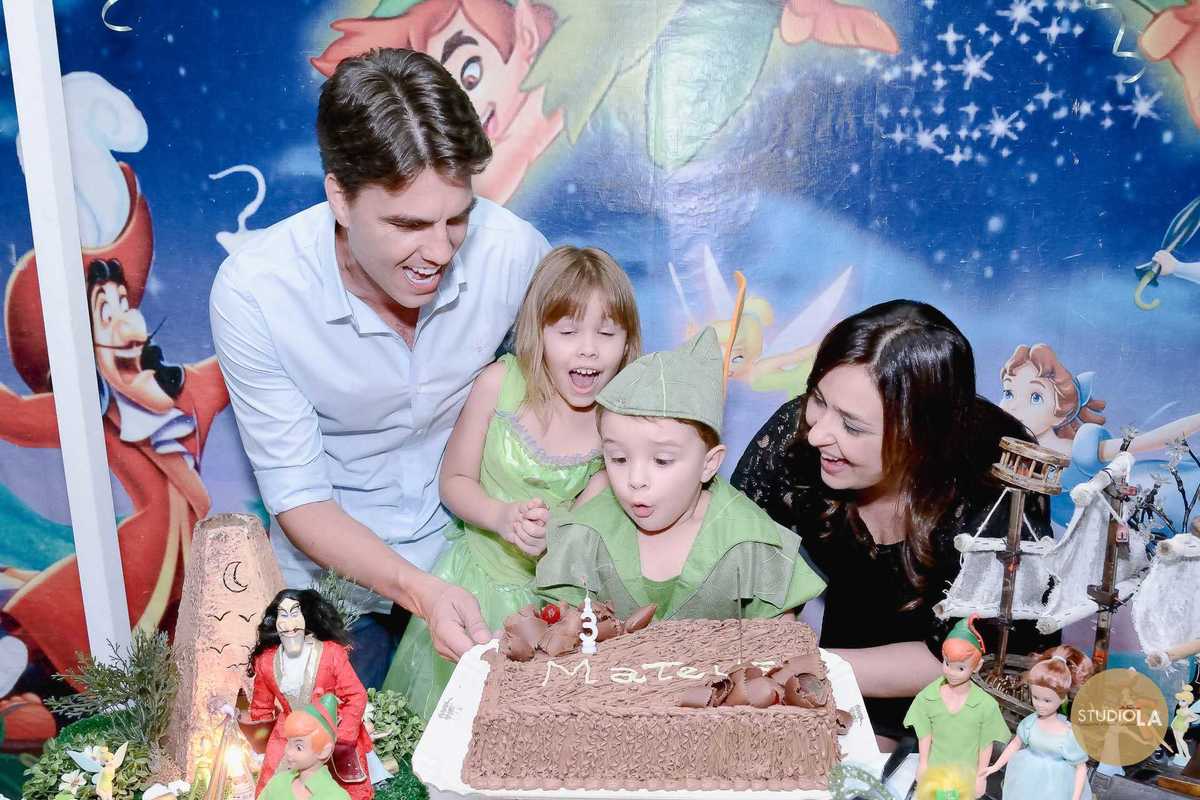 A emoção de apagar a velinha registrada no instante perfeito: aniversariante fantasiado de Peter Pan, cercado pela família e amigos. Foto de festa infantil feita pelo Studio LA.
