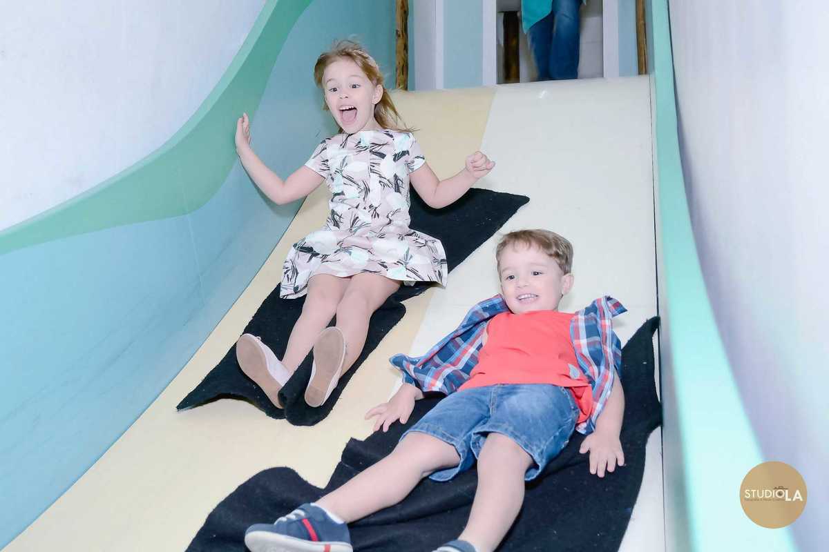 Fotografia divertida dos irmãos descendo no escorregador durante a festa infantil no Buffet Feliz da Vida em São Paulo, feita pelo Studio LA.