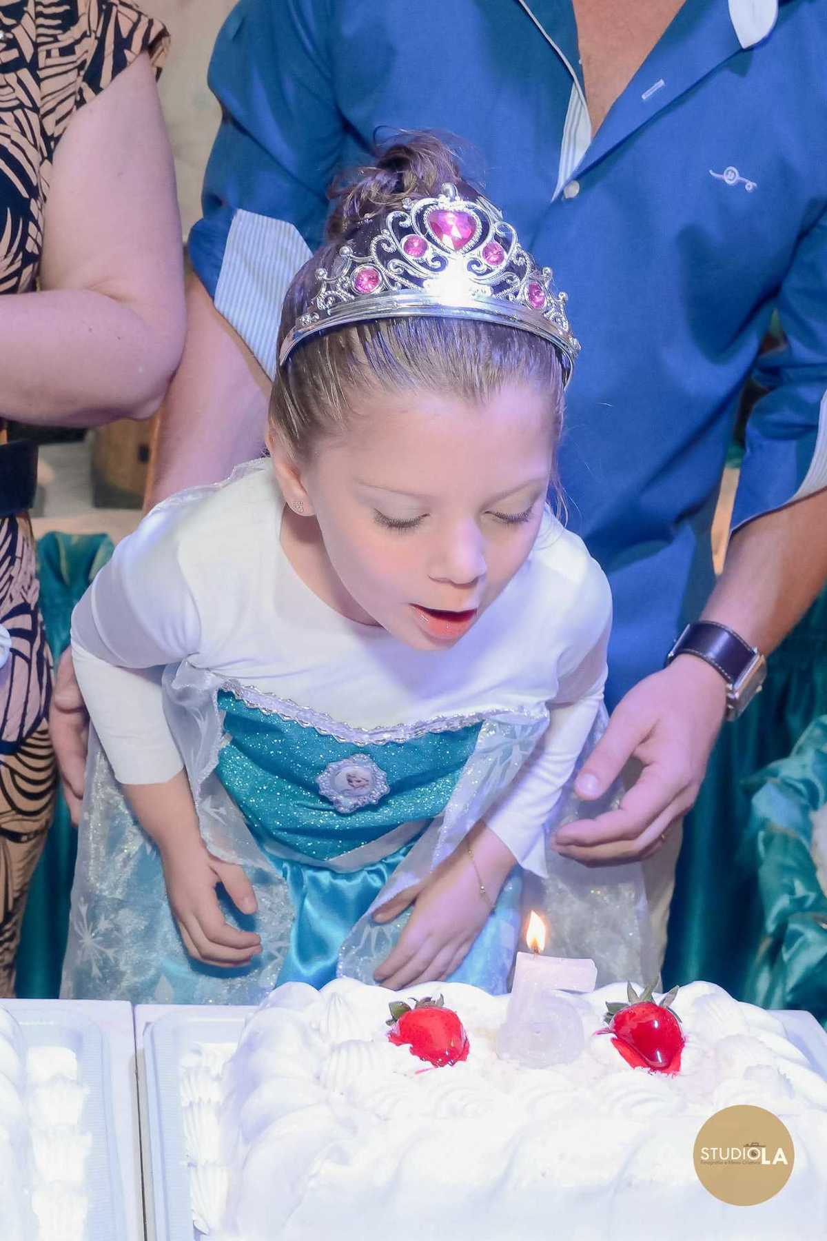 Hora do parabéns com aniversariante soprando a vela em seu bolo temático Frozen, em festa infantil no buffet em São Paulo. Foto emocionante feita pelo Studio LA.