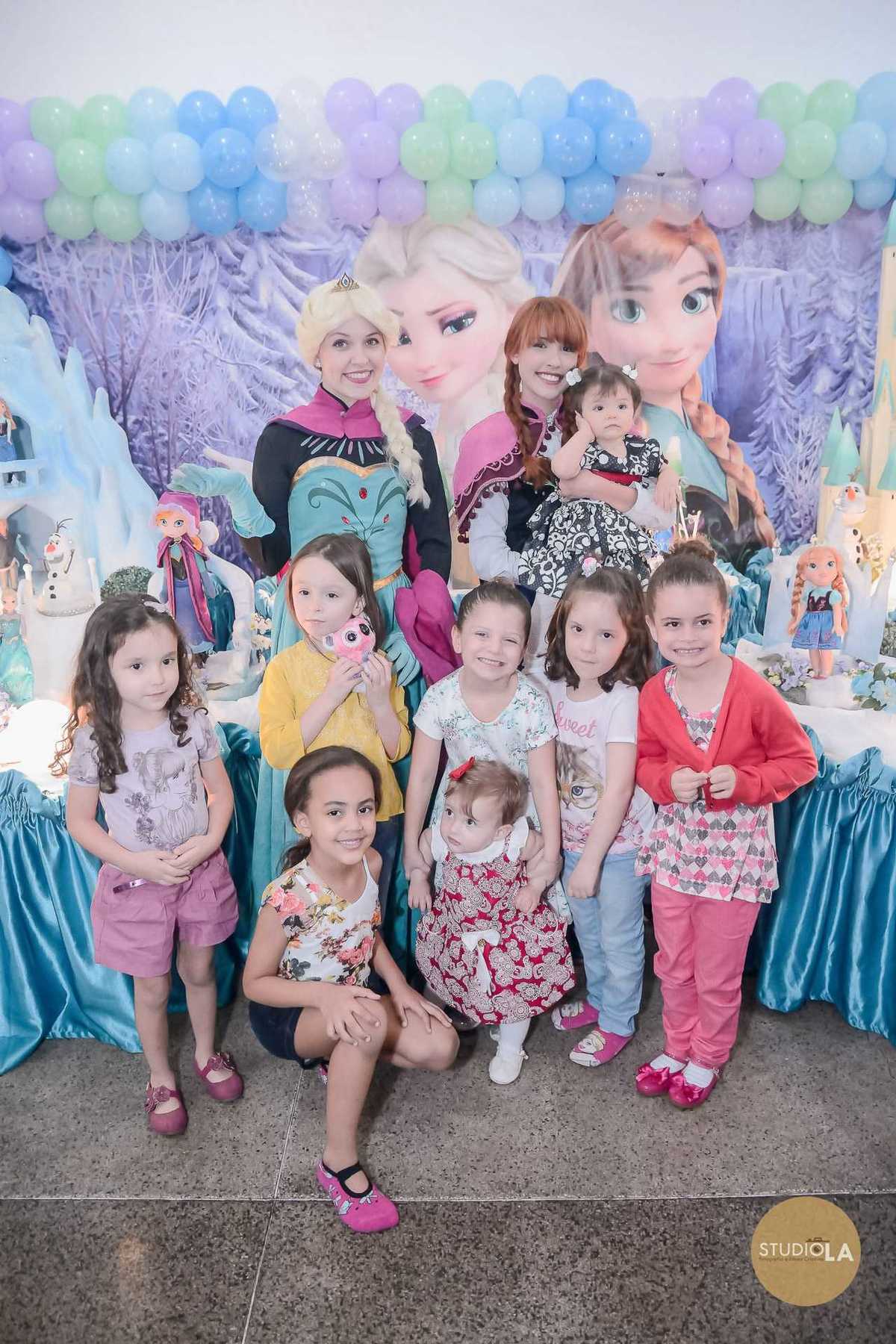 Grupo de crianças e personagens da Frozen reunidos para foto especial em frente à mesa decorada de aniversário infantil. Momento único registrado pelo Studio LA.