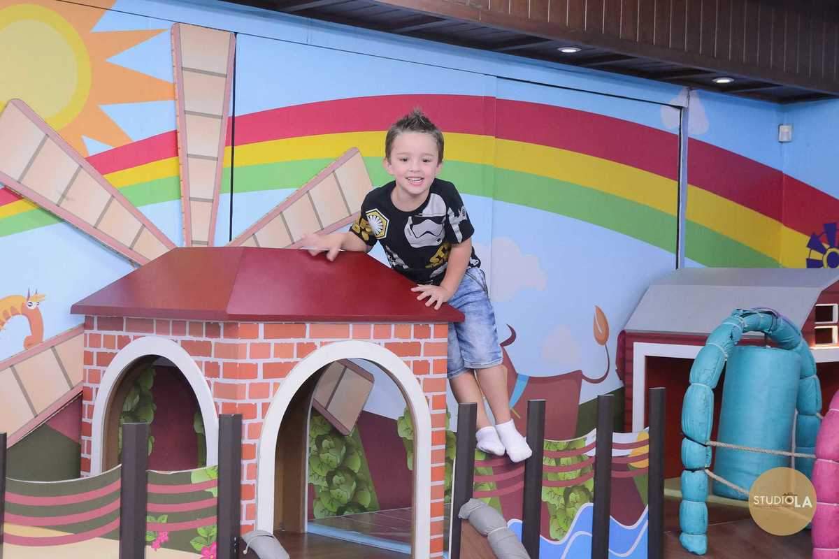 Criança sorridente se divertindo em brinquedo colorido com arco-íris no fundo durante festa infantil em São Paulo — Fotografia de aniversário infantil por Studio LA.