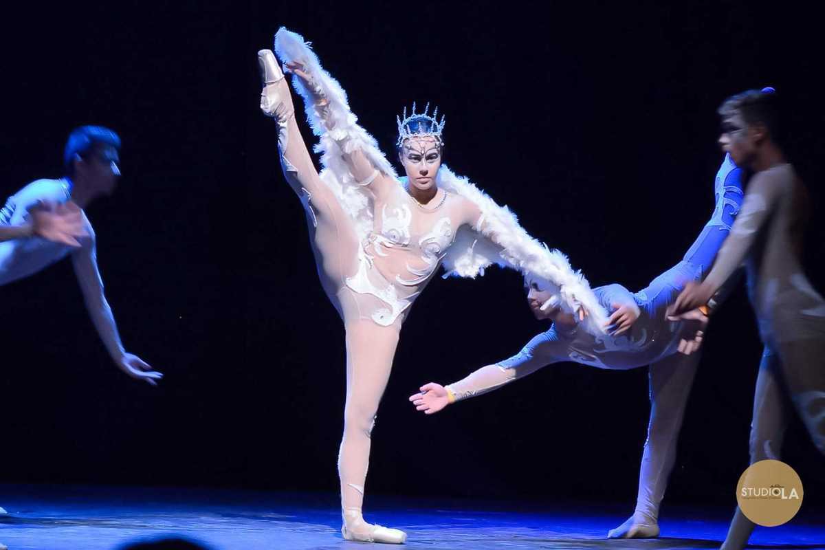 Fotografia de apresentação de dança com bailarina em figurino azul e branco, braços erguidos em pose graciosa. Foto profissional do Studio LA em espetáculo teatral e de balé.