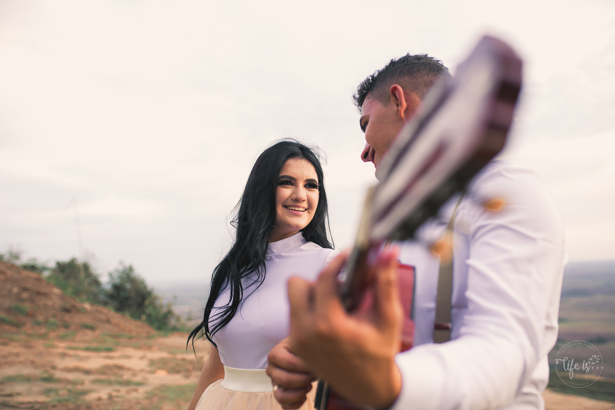 O olhar da noiva enquanto o noivo toca o violão em ensaio casal