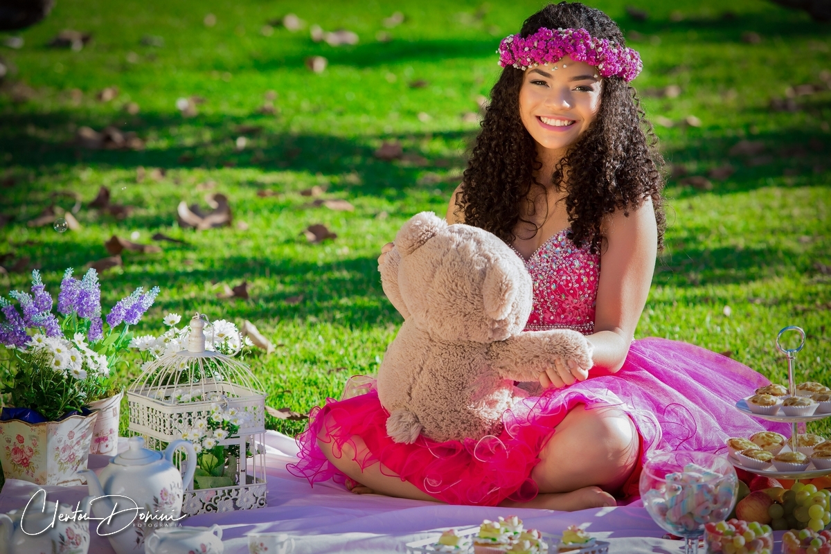 MENINA SENTADA NA GRAMA SEGURANDO UM  URSO DE PELÚCIA 