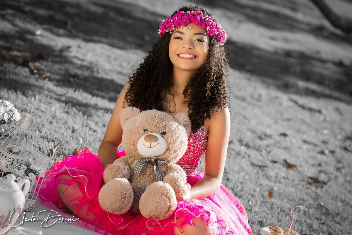 MENINA SENTADA NA GRAMA SEGURANDO UM  URSO DE PELÚCIA 