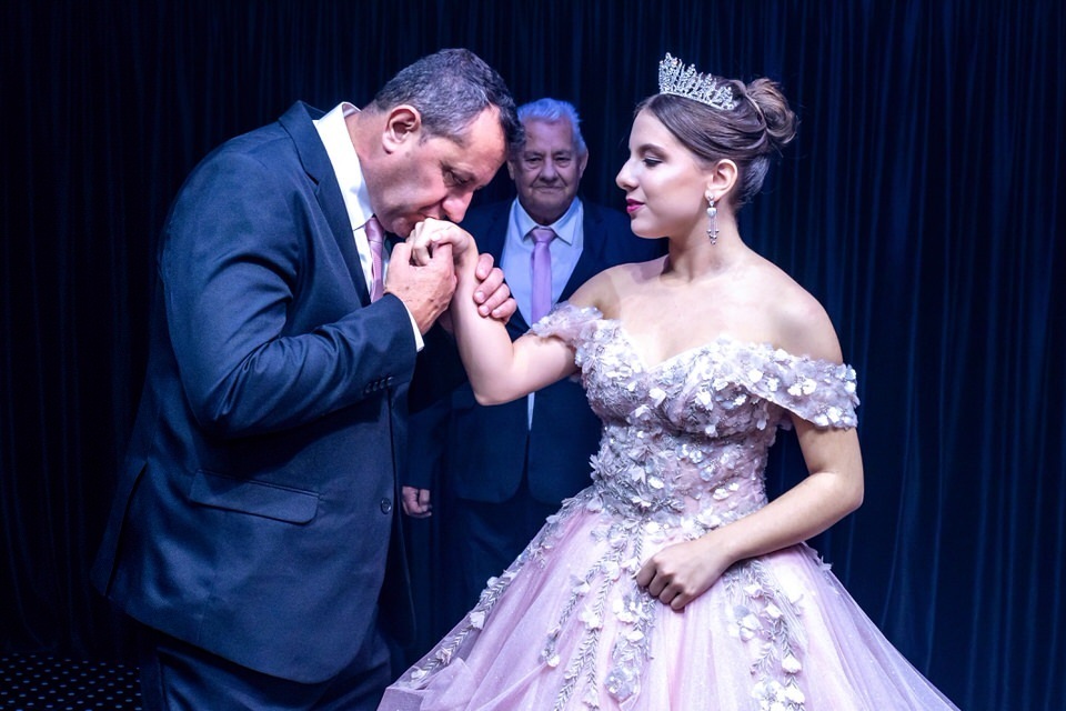 Momento emocionante do pai beijando a mão da debutante Roberta após a entrega do anel. Cobertura fotográfica de festa de 15 anos em SP.