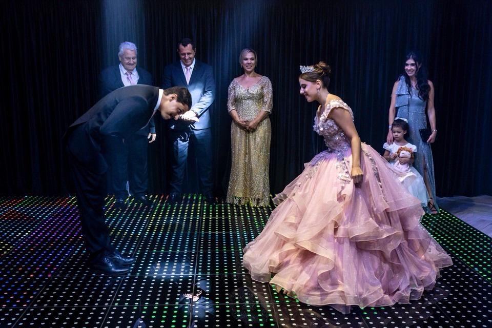 Irmão da debutante Roberta faz a reverência para iniciar a dança na festa de 15 anos. Fotografia de momentos especiais por fotógrafo de debutante em São Paulo.