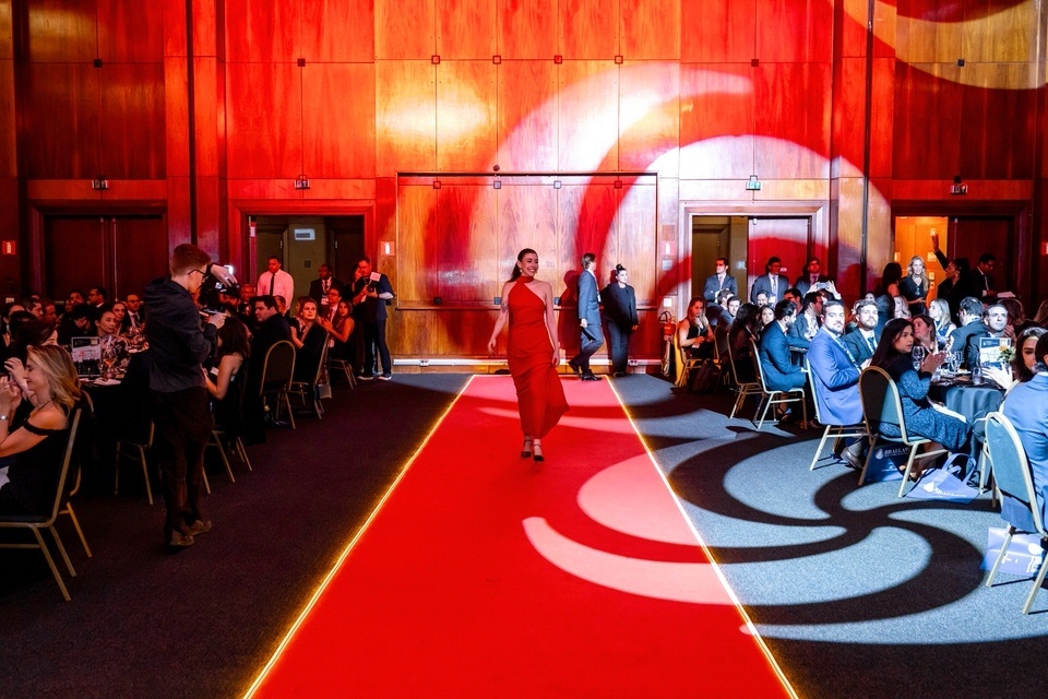 Registro de evento jurídico com convidada desfilando pelo tapete vermelho iluminado no salão do BRALLAW Awards no WTC São Paulo.
