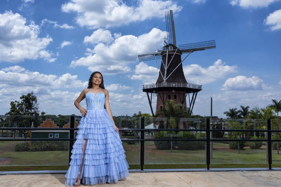 Fotógrafo de debutante em Holambra registra jovem com vestido azul em frente ao moinho Povos Unidos.