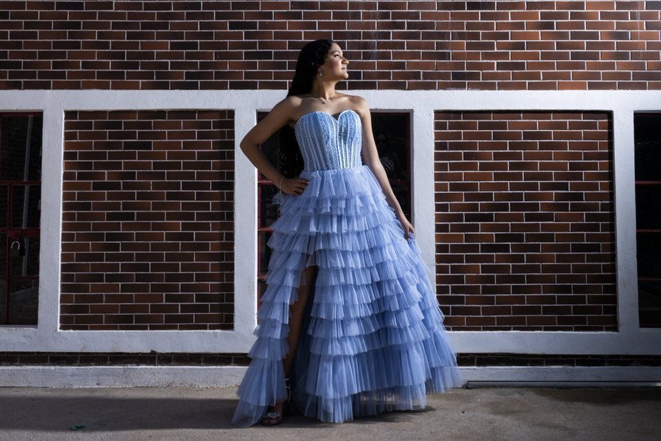 Fotógrafo de debutante em Holambra cria retrato moderno de jovem com vestido azul em frente a uma parede de tijolos.