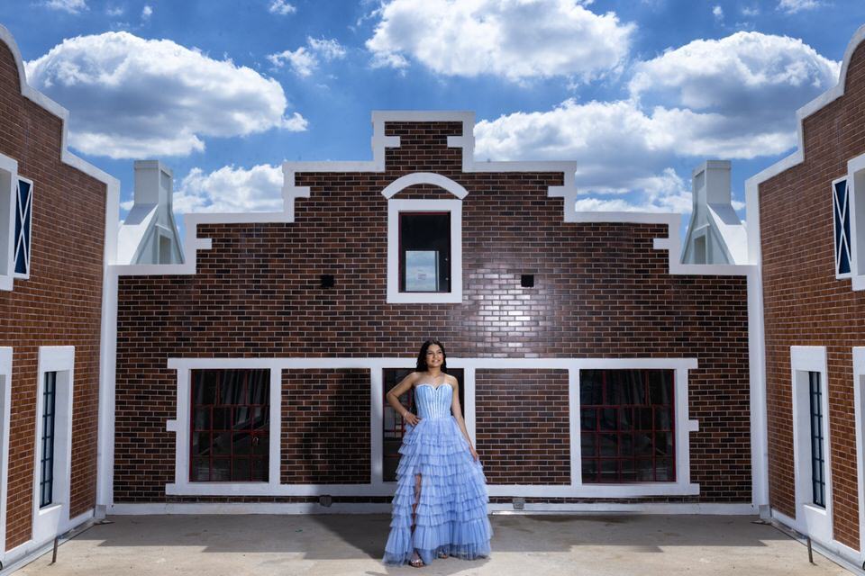 Fotógrafo de debutante em Holambra posiciona jovem com vestido azul em frente a uma fachada de arquitetura holandesa.