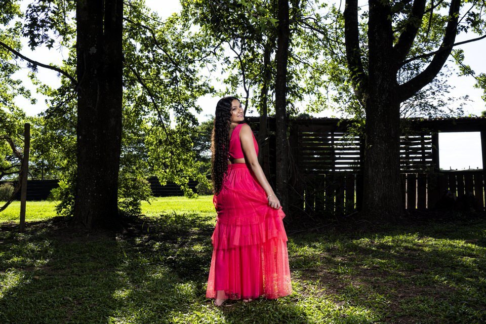 Fotógrafo de debutante em Holambra captura a alegria de jovem com vestido pink vibrante em um ensaio ao ar livre, cercada por árvores.