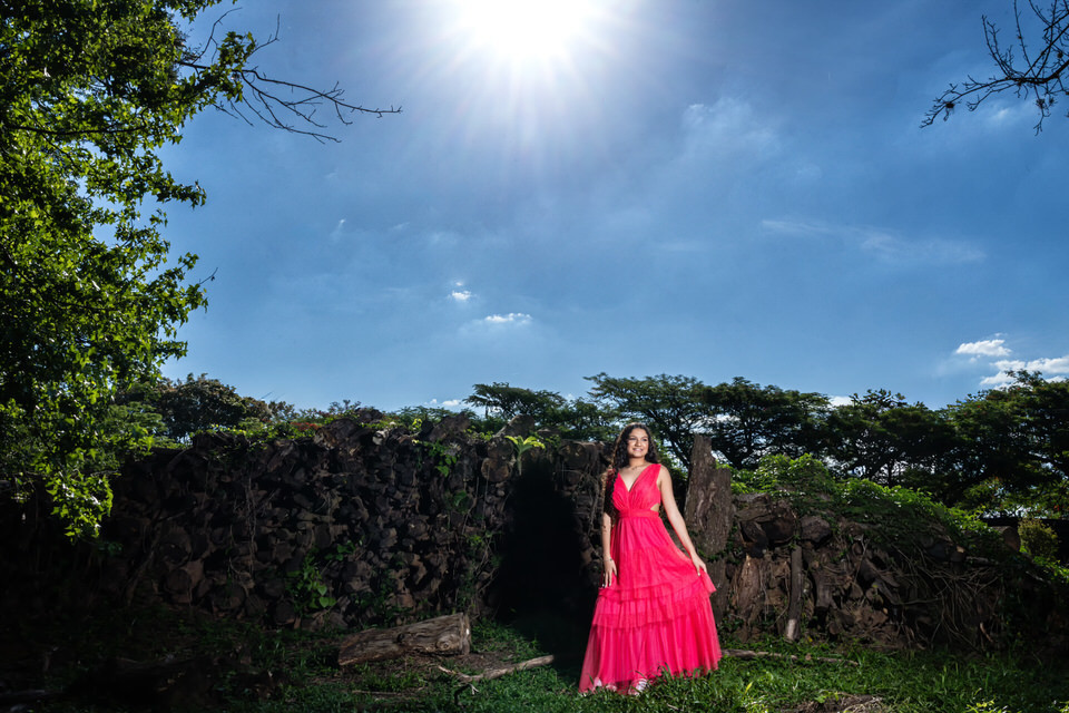 Fotógrafo de debutante em Holambra em ensaio no Macena Flores, com jovem de vestido pink em frente a uma estrutura rústica sob o sol forte.