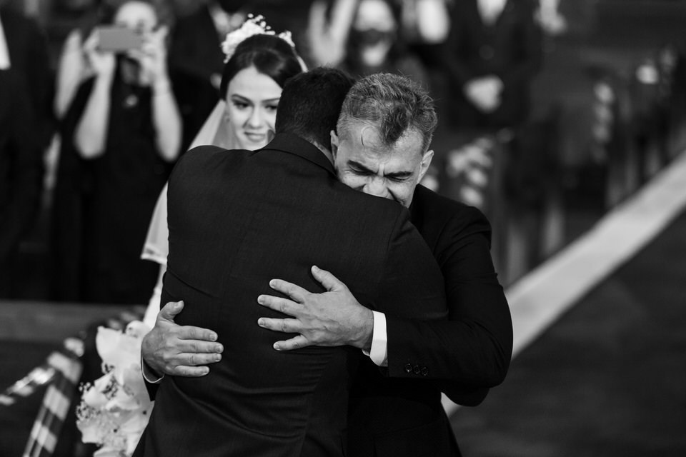 Pai da noivo abraçando o noivo na igreja matriz Sagrada Família, Noivo esperando a noiva no altar, momento registrado pelo fotógrafo de casamentos John Edgard  em São Bernardo do Campo - SP