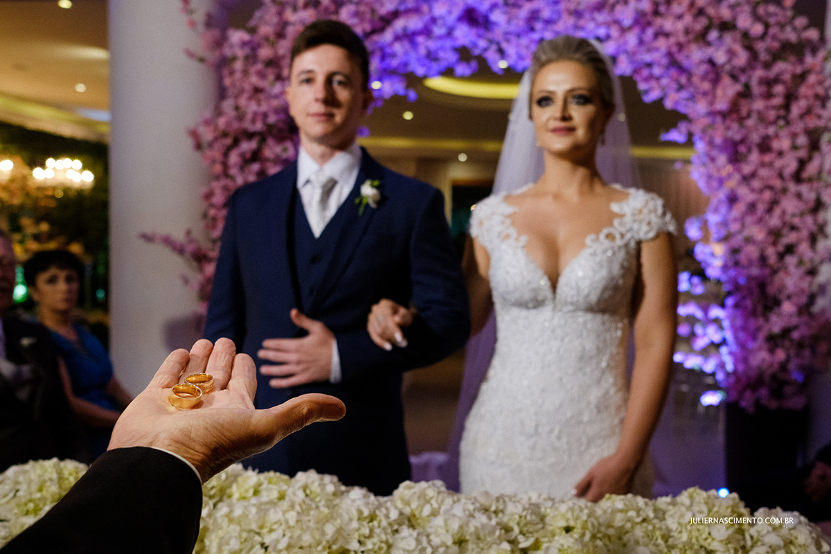 Foto de alianças de casamento com os noivos as fundo