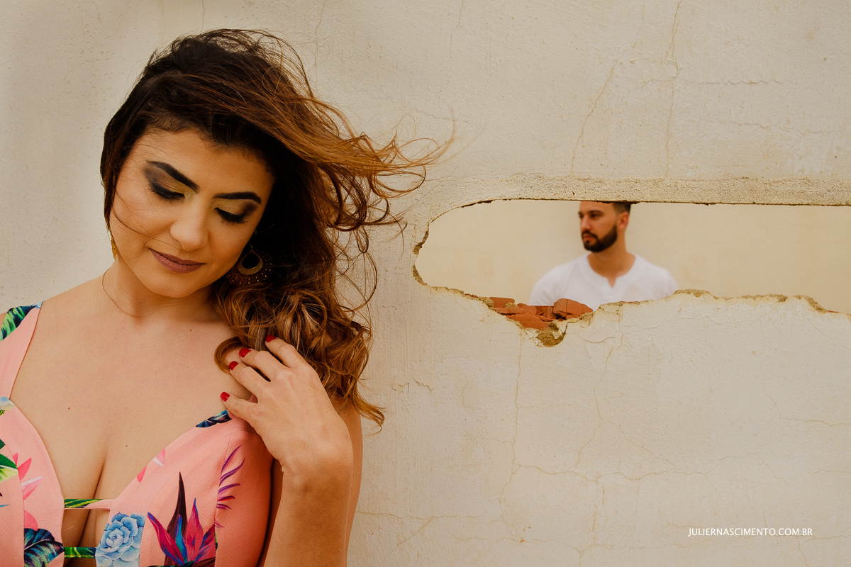 noiva mexendo no cabelo e noivo no fundo no ensaio pré casamento