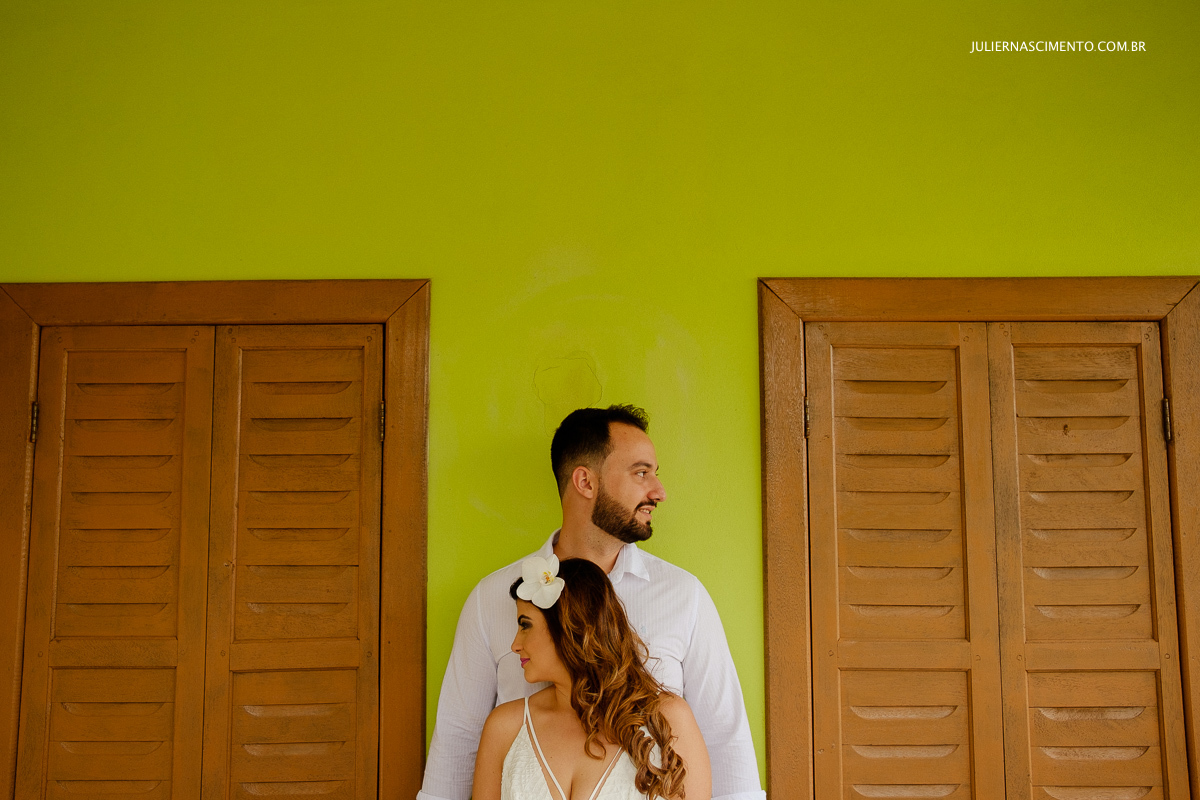 casal encostados numa parede verde no seu ensaio pré casamento