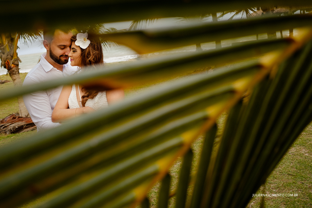 casal abraçado entre as folhas de coqueiros em frente ao mar