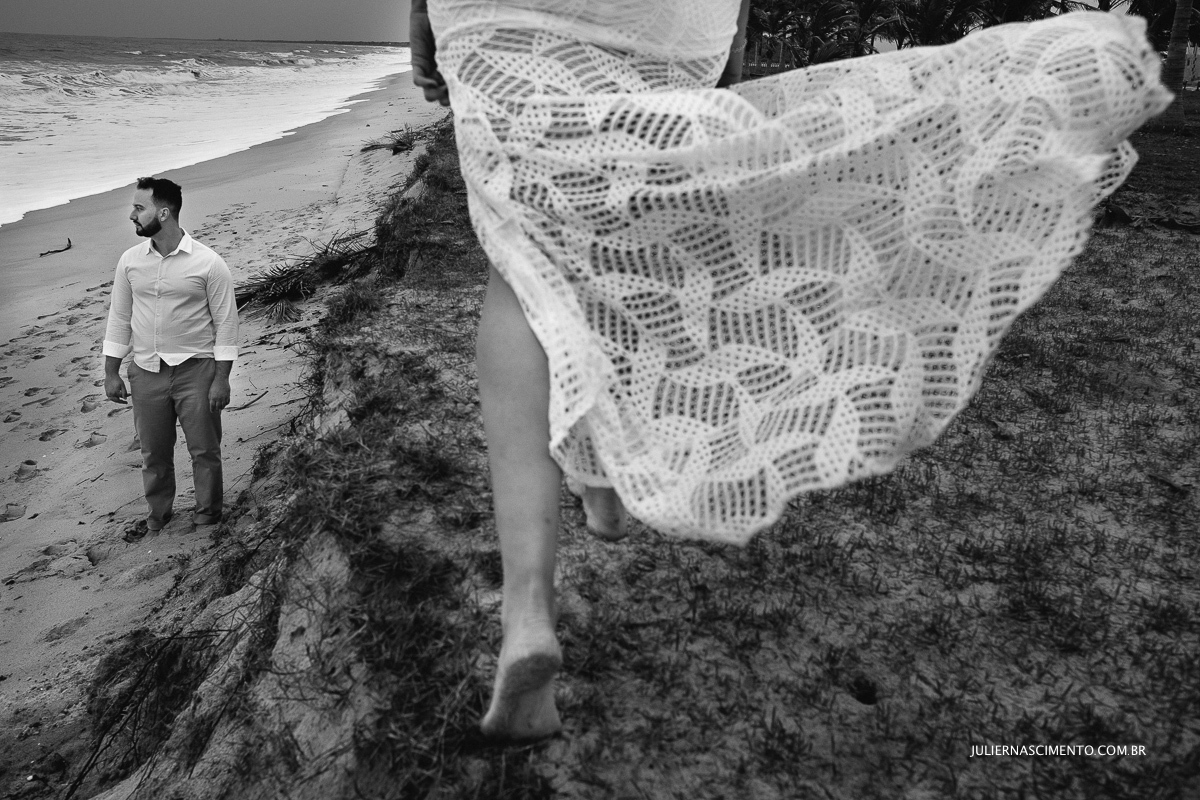 foto preto e branco de detalhe dos pés de mulher andando e noivo no fundo próximo ao mar em ensaio esession