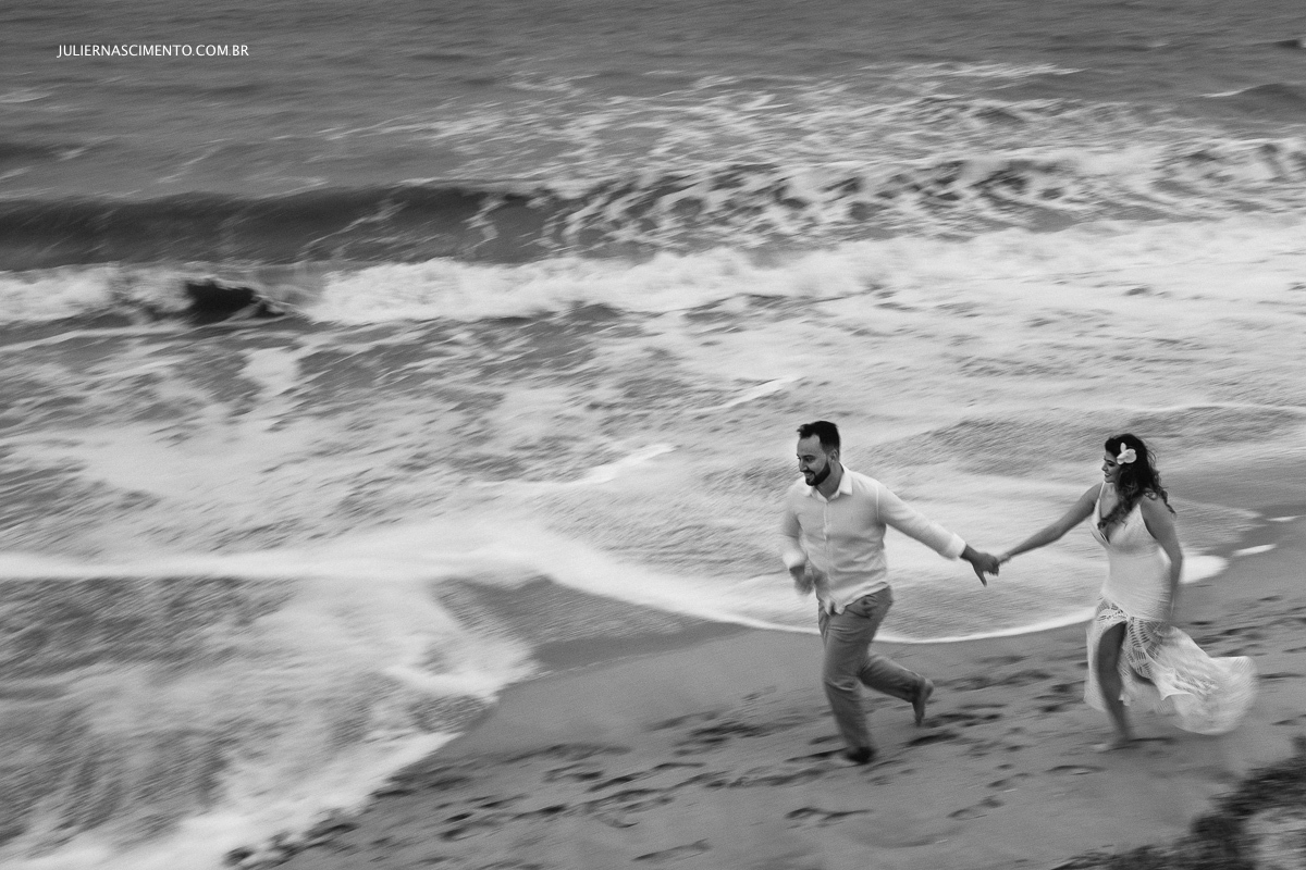 Noivos correndo em frente ao mar na praia de nova viçosa na Bahia