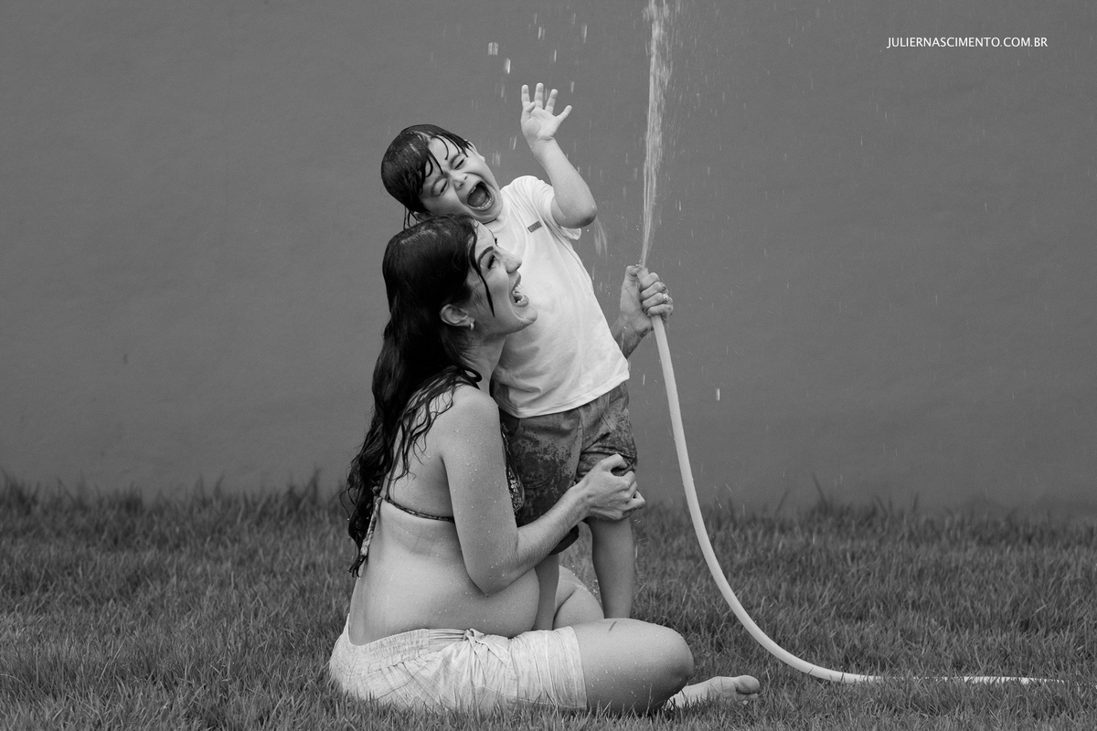 foto preto e branco de grávida com seu filho brincando com mangueira de água