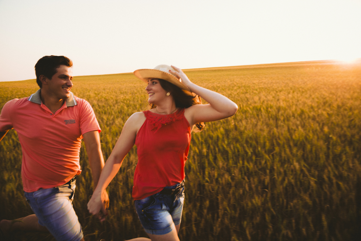 pré casamento casal correndo no trigo de chapéu felicidade olho no olho por do sol