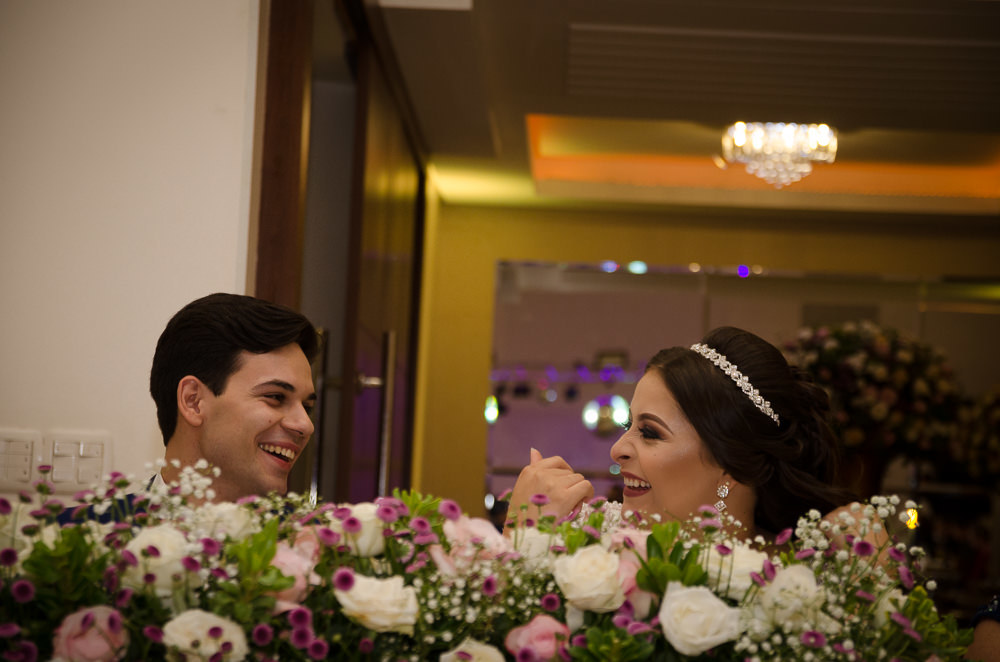 Fotografia da recepção ou festa de casamento dos noivos sentados e sorrindo e flores brancas e coloridas como decoração da mesa no espaço de eventos em Maringá PR