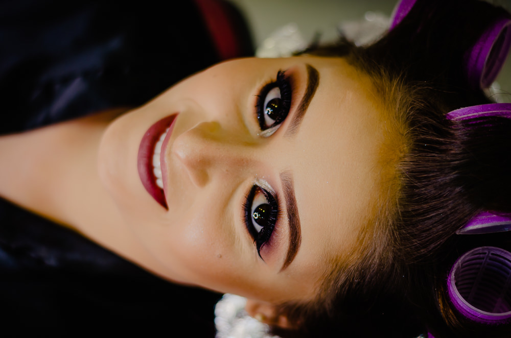 Fotografia na noiva no making of no dia do casamento no salão de beleza no dia da noiva fazendo a maquiagem olhando para câmera e sorrindo em Maringá PR