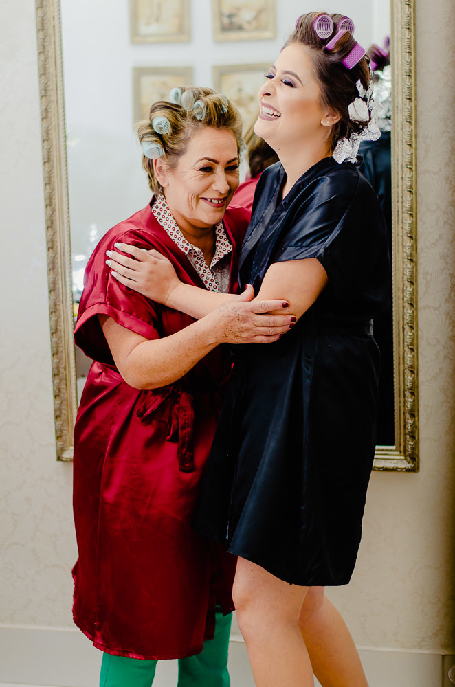 Fotografia na noiva no making of no dia do casamento no salão de beleza no dia da noiva de roupão abraçando sua mãe em Maringá PR