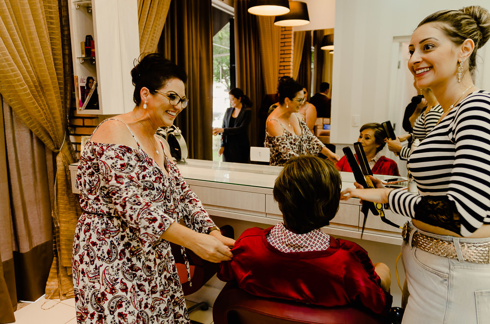 Fotografia de making of no dia do casamento no salão de beleza no dia da noiva de sua mãe arrumando o cabelo e uma amiga da família em Maringá PR