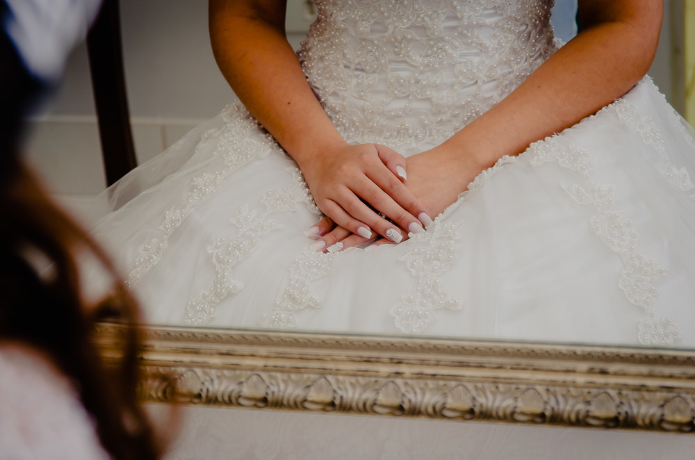 Fotografia de making of no dia do casamento no salão de beleza no dia da noiva. A noiva em frente ao espelho sentada, foto apenas de suas mãos em Maringá PR