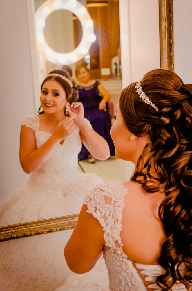 Fotografia de making of no dia do casamento no salão de beleza no dia da noiva em frente ao espelho com cabelo e maquiagem prontos uma tiara no cabole e arrumando os brincos em Maringá PR