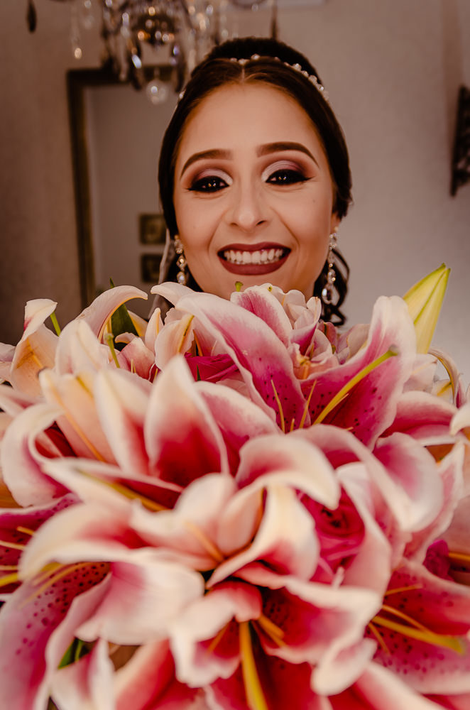 Fotografia de making of no dia do casamento no salão de beleza no dia da noiva ela sorrindo com o buquê ou buquet