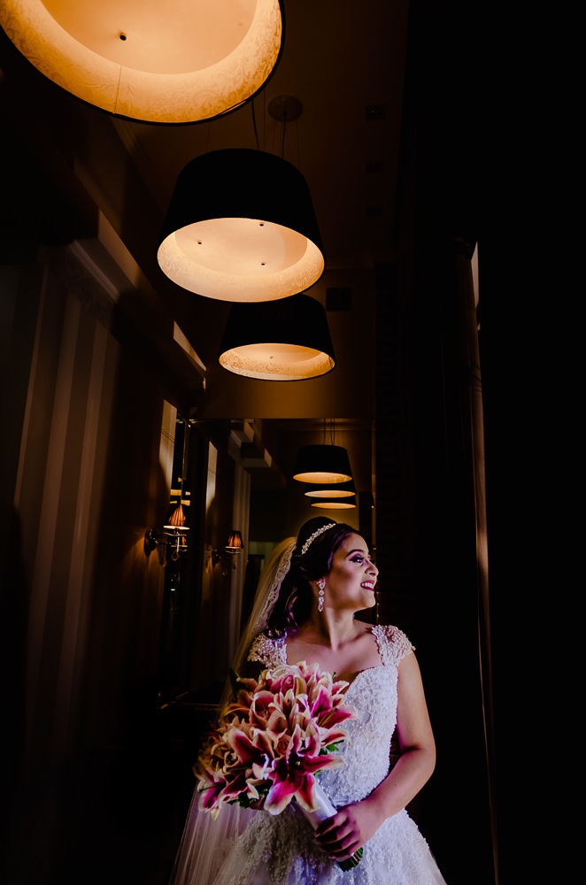 Fotografia de making of no dia do casamento no salão de beleza no dia da noiva de corpo inteiro iluminada com luz natural com vestido de noiva branco tiara no cabelo, véu de noiva e brincos em Maringá PR