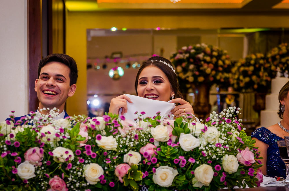 Fotografia da recepção ou festa de casamento dos noivos sentados e sorrindo e flores brancas e coloridas como decoração da mesa no espaço de eventos em Maringá PR
