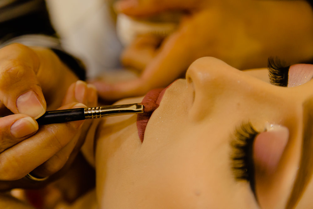 Fotografia do making of da noiva no dia do casamento no salão de beleza fazendo a maquiagem passando o batom em Maringá PR