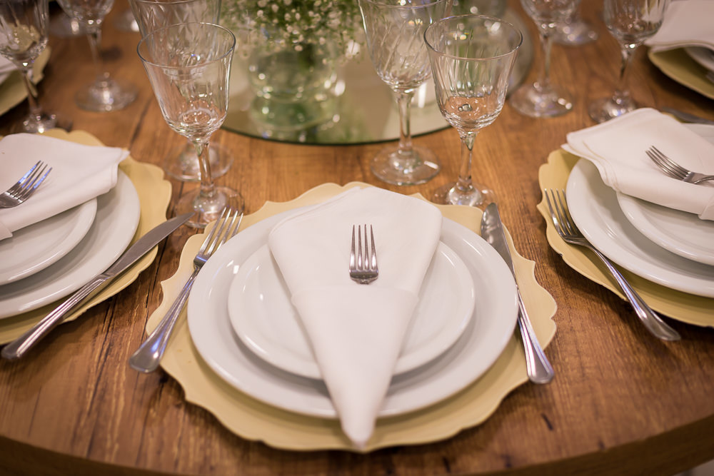 Fotografia da decoração do dia do casamento da mesa de jantar com os pratos, talheres, taças e flores sobre a mesa no salão de festas em Maringá PR