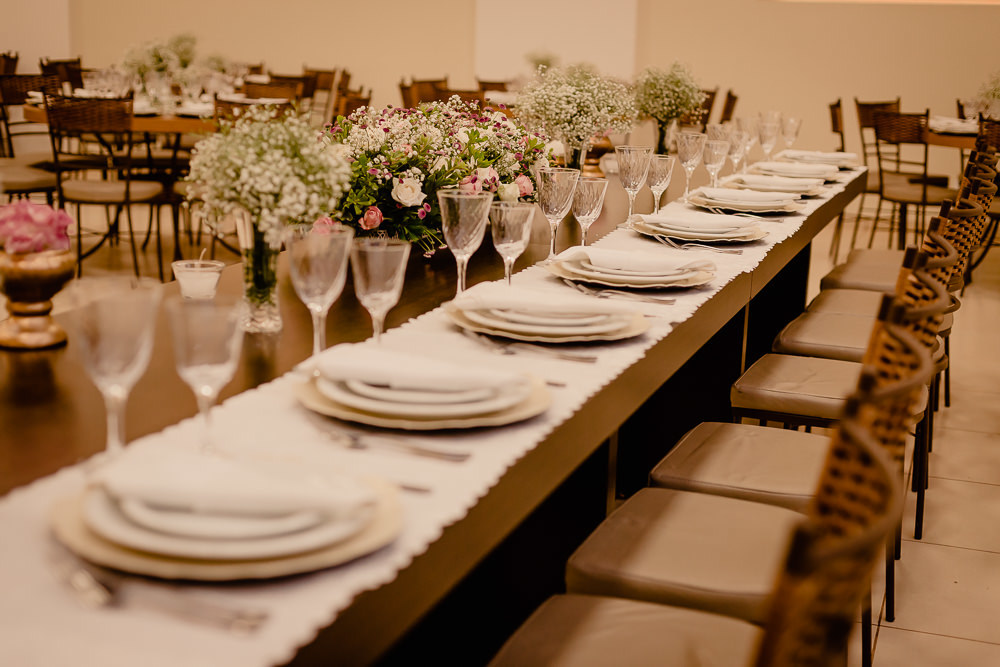 Fotografia de decoração da festa e recepção de casamento no salão ou espçao de eventos da mesa de convidados especiais com a decoração de flores, taças, pratos, talheres, guardanapos e as cadeiras no salão de eventos em Maringá PR