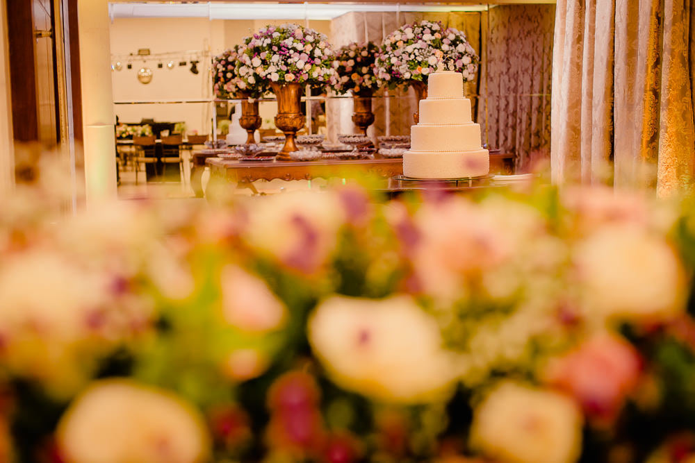 Fotografia do dia do casamento de decoração no salão ou espaço de eventos de festas no dia da recepção com a decoração de flores naturais com a mesa de doces decorada e Bolbo de Casamento ao fundo no espaço de eventos em Maringá PR