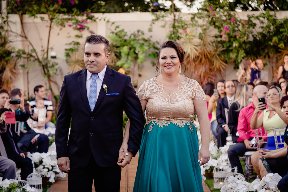 Fotografia da cerimônia de casamento na nave com os convidados e os pai e a mãe do noivo entrando e sorrindo no espaço de eventos em Mariná PR