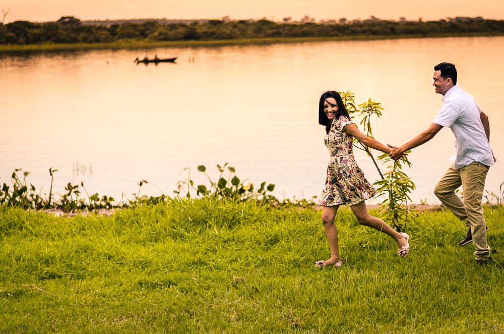 Fotografia com o rio Tietê no por do sol do noivo e da noiva no ensaio pre casamento ou wedding correndo de mãos dadas e sorrindo em Araçatuba, SP