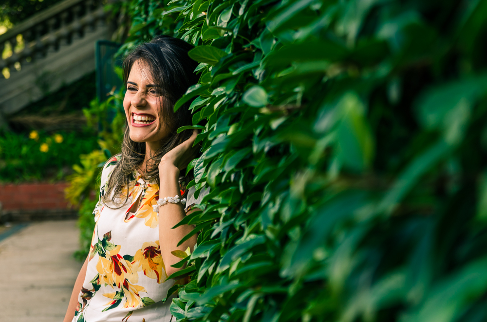 Foto do ensaio pre wedding, casamento da noiva em um muro de folhas verdes sorrindo feliz num dia de sol. Parque do Ipiranga, São Paulo, Brasil.