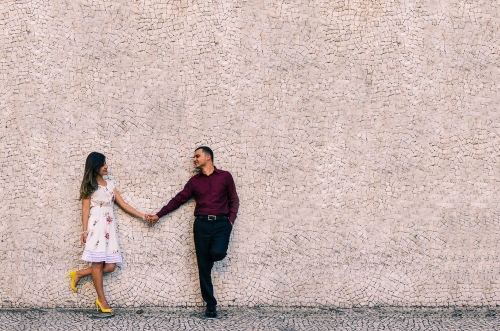 Foto do ensaio pre casamento, wedding do casal de noivos de mãos dadas trocando olhares frente a um paredão de pedras brancas. O noivo e a noiva estão no Bairro Liberdade, São Paulo, Brasil.