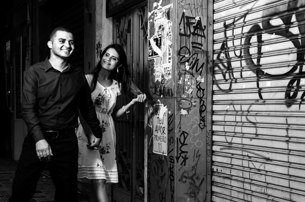 Foto noturna em preto e branco, pb, do ensaio pre casamento, wedding do casal de noivos caminhando de mais dadas na rua a noite. O noivo e a noiva estão no Bairro Liberdade, São Paulo, Brasil.