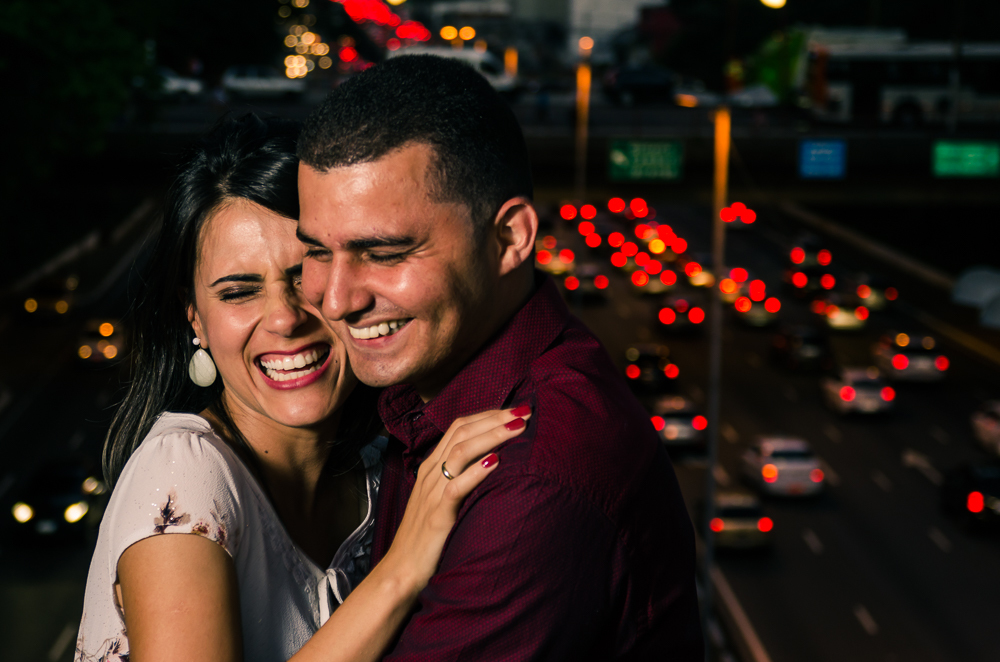 Foto noturna do Ensaio pre Casamento, Wedding do casal de noivos de mãos dadas em cima da ponte com avenida movimentada ao fundo, a noite. O noivo e a noiva estão no Bairro Liberdade, São Paulo, Brasil.