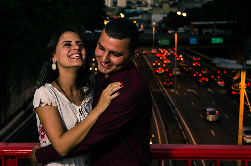 Foto noturna do Ensaio pre Casamento, Wedding do casal de noivos de mãos dadas em cima da ponte com avenida movimentada ao fundo, a noite. O noivo e a noiva estão no Bairro Liberdade, São Paulo, Brasil.