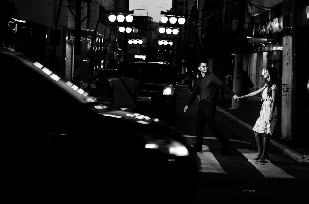 Foto noturna em preto e branco, pb, do ensaio pre casamento, wedding do casal de noivos caminhando de mais dadas na rua a noite. O noivo e a noiva estão no Bairro Liberdade, São Paulo, Brasil.