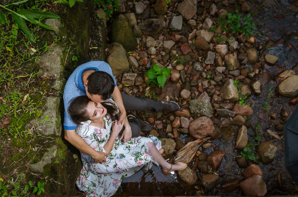 Foto do ensaio pre wedding, casamento, do casal ao ar livre no riacho com cascalhos na vegetação verde no Hotel Capo Zorial com piscina e monte ao fundo no Recanto do Maestro em São João do Polêsine, RS, próximo de Santa Maria, RS